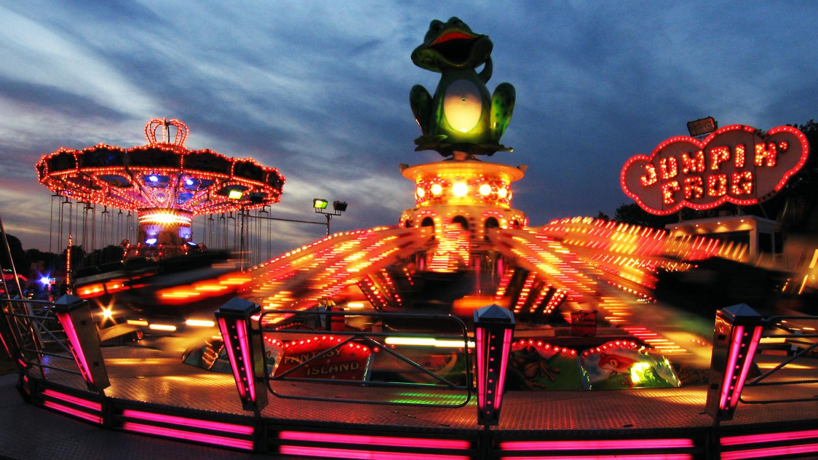 Beleuchtete Fahrgeschäfte einer Kirmes im Abendrot