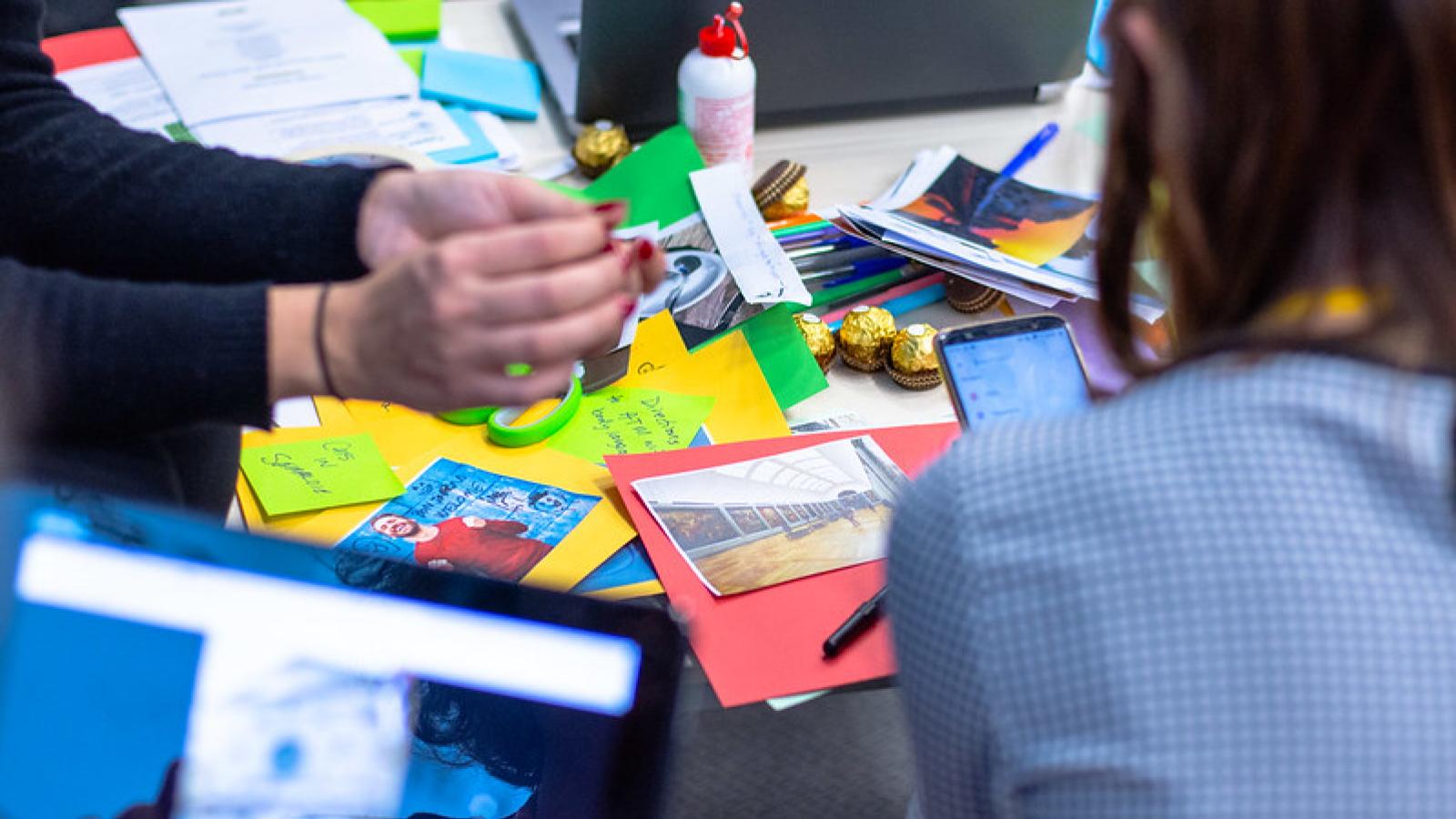 Workshop-Situation; Menschen sitzen am Tisch und gestalten gemeinsam eine Collage