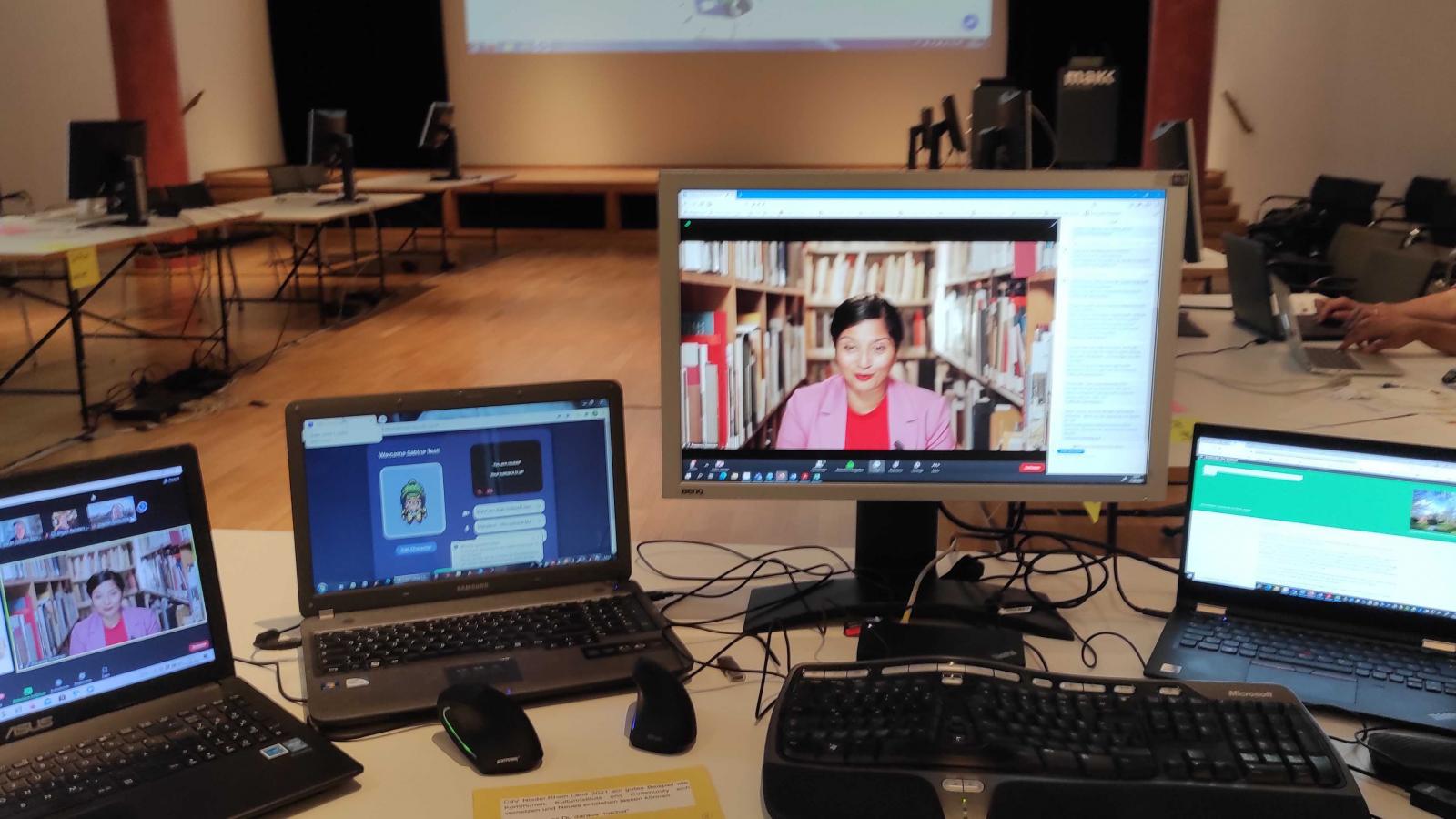 Foto des Overstolzen-Saals im MAKK mit der "Kommandozentrale" – vier Monitoren auf denen jeweils eines der für den Kick-Off verwendeten Tools (Zoom, Gather.Town, Slack und Twitter) zu sehen sind.wurde