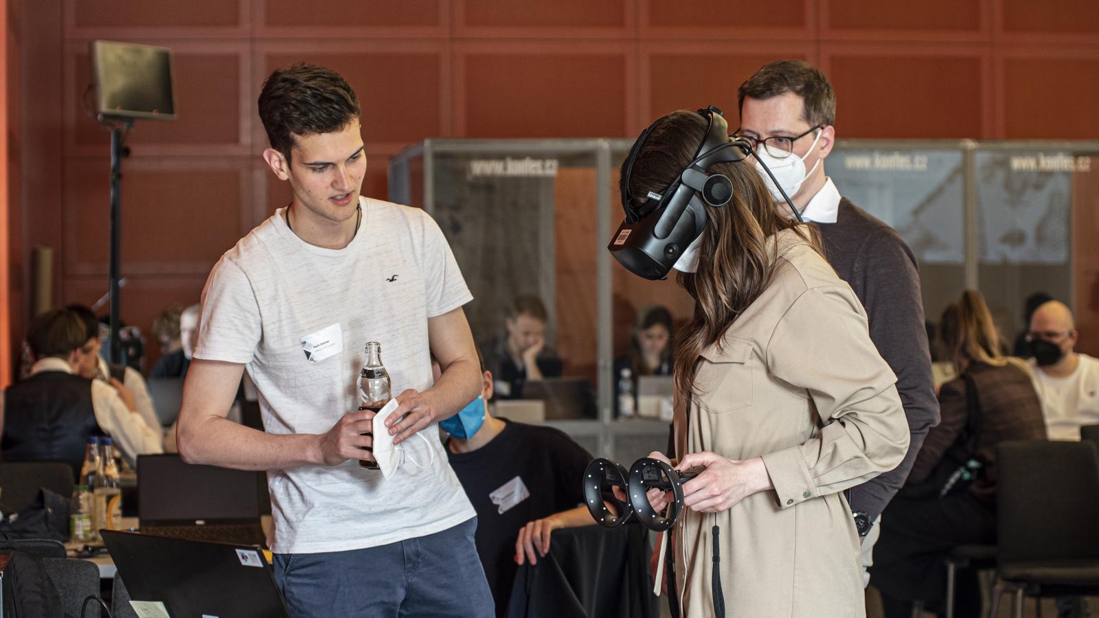 Eine Teilnehmerin der Preisverleihung von Coding da Vinci Ost³ 2022 testet mit einer Virtual Reality Brille ein Projekt aus. Der Entwickler des Projekts erklärt ihr die Funktionsweise.