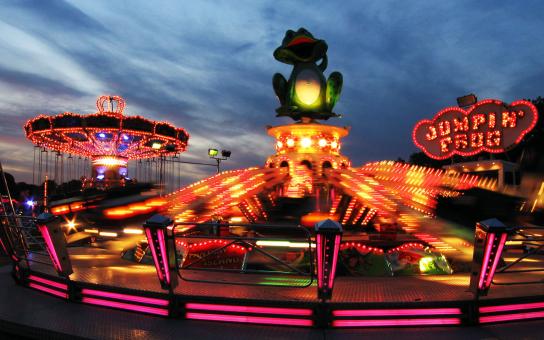 Beleuchtete Fahrgeschäfte einer Kirmes im Abendrot