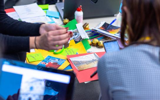 Workshop-Situation; Menschen sitzen am Tisch und gestalten gemeinsam eine Collage