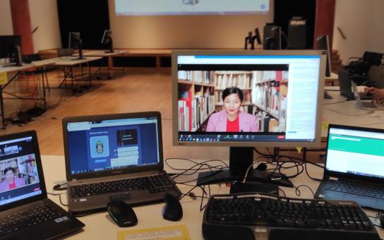Foto des Overstolzen-Saals im MAKK mit der "Kommandozentrale" – vier Monitoren auf denen jeweils eines der für den Kick-Off verwendeten Tools (Zoom, Gather.Town, Slack und Twitter) zu sehen sind.wurde