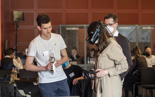 Eine Teilnehmerin der Preisverleihung von Coding da Vinci Ost³ 2022 testet mit einer Virtual Reality Brille ein Projekt aus. Der Entwickler des Projekts erklärt ihr die Funktionsweise.